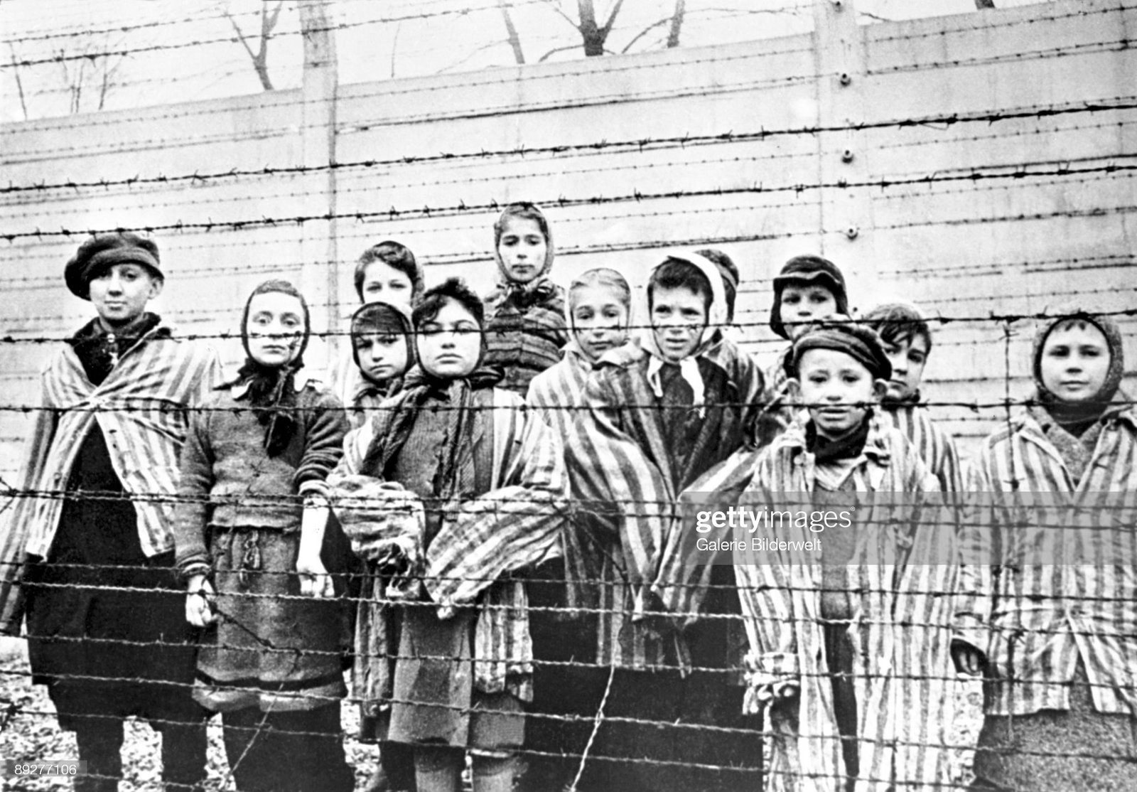 A group of child survivors behind a barbed wire fence at the Nazi concentration camp at Auschwitz-Birkenau in southern Poland, on the day of the camp’s liberation by the Red Army, 27th January 1945. Photo taken by Red Army photographer Captain Alexander Vorontsov during the making of a film about the liberation of the camp. The children were dressed in adult uniforms by the Russians. The children are (left to right): Tomy Schwarz (later Shacham), Miriam Ziegler, Paula Lebovics (front), Ruth Webber, Berta Weinhaber (later Bracha Katz), Erika Winter (later Dohan), Marta Weiss (later Wise), Eva Weiss (later Slonim), Gabor Hirsch (just visible behind Eva Weiss), Gabriel Neumann, Robert Schlesinger (later Shmuel Schelach), Eva Mozes Kor, and Miriam Mozes Zeiger. (Photo by Alexander Vorontsov/Galerie Bilderwelt/Getty Images)